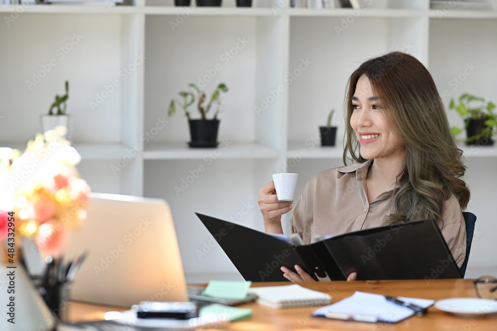 Positive asian woman drinking coffee and looking out of window.