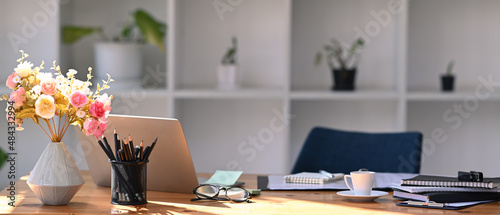 Comfortable workplace with laptop computer, flower pot, coffee cup and office supplies.