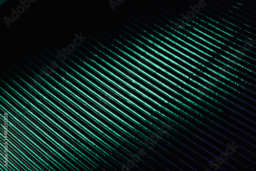 Corrugated texture. Neon light background. Grooved metal surface. Fluorescent green color gradient glow reflection on parallel lines pattern dark black abstract overlay.