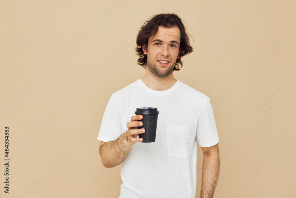 Attractive man in a white T-shirt with a black glass in hand Lifestyle unaltered Attractive man in a white T-shirt with a black glass in hand Lifestyle unaltered