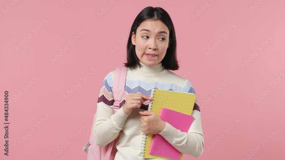 Confused fun girl teen student of Asian ethnicity 20s wears shirt backpack hold books spreading hands say oops ouch oh omg i am so sorry isolated on plain pastel light pink background studio portrait Confused fun girl teen student of Asian ethnicity 20s wears shirt backpack hold books spreading hands say oops ouch oh omg i am so sorry isolated on plain pastel light pink background studio portrait