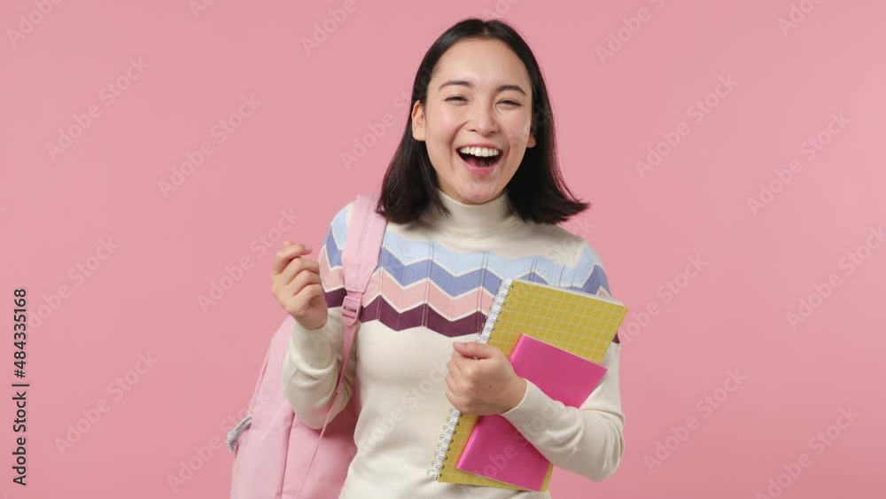 Curious nosy smiling fun girl teen student of Asian ethnicity 20s wears shirt backpack hold books try to hear you overhear show thumb up isolated on plain pastel light pink background studio portrait Curious nosy smiling fun girl teen student of Asian ethnicity 20s wears shirt backpack hold books try to hear you overhear show thumb up isolated on plain pastel light pink background studio portrait