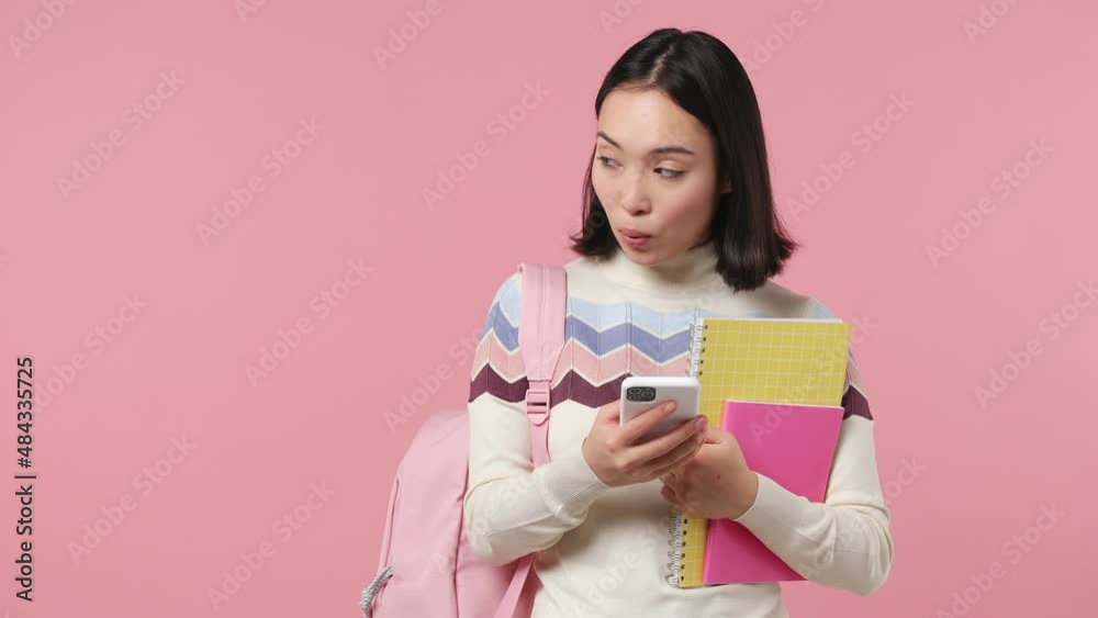 Girl teen student of Asian ethnicity wear shirt backpack hold books use mobile cell phone look aside on workspace area copy space mock up isolated on plain pastel light pink background studio portrait Girl teen student of Asian ethnicity wear shirt backpack hold books use mobile cell phone look aside on workspace area copy space mock up isolated on plain pastel light pink background studio portrait