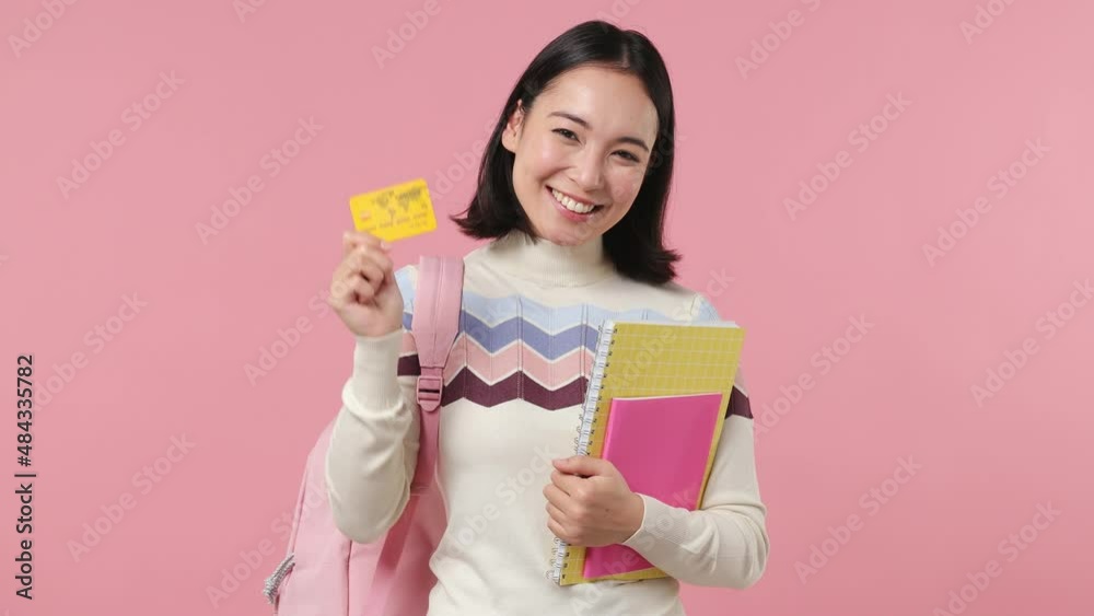 Girl teen student of Asian ethnicity wear shirt backpack hold books credit bank card isolated on plain pastel light pink background studio portrait. Education in high school university college concept Girl teen student of Asian ethnicity wear shirt backpack hold books credit bank card isolated on plain pastel light pink background studio portrait. Education in high school university college concept