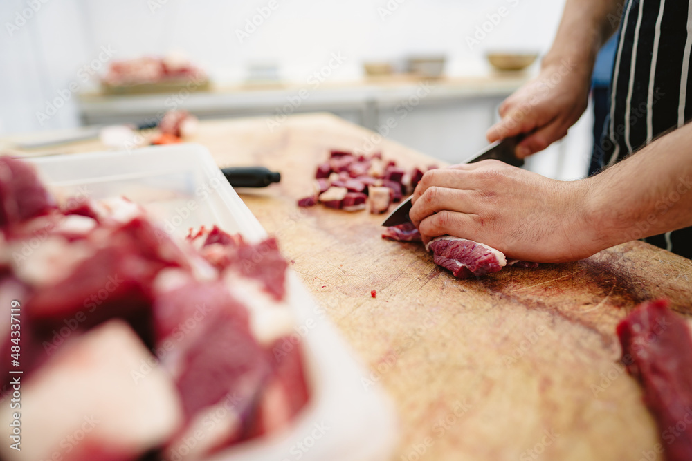 Butcher cutting slices of raw meat on wooden board