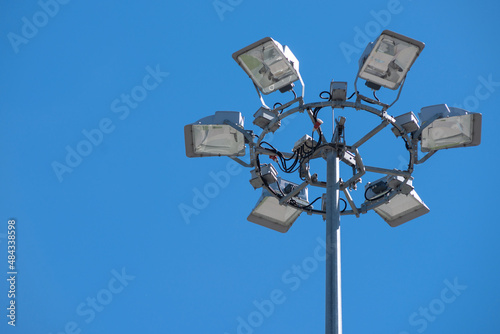 Projector stand made of several individual spotlights on the background of blue clear limitless sky. Lighting mast concept at the stadium, construction site or plant. Copy space for text