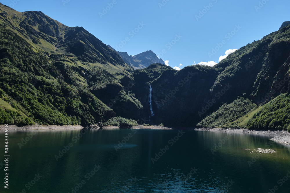 Lac d'Oô in the French Pyrenees is an artificial lake surrounded by large green mountains with a large waterfall.