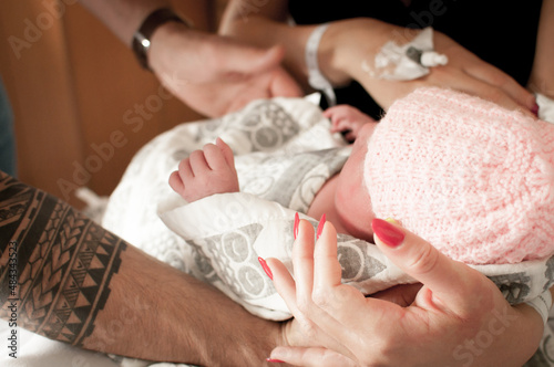 Close up of a father   s tattooed arm and her partners    hand with red nails holding their newborn baby daughter wearing a pink hat wrapped up in a blanket in a flat in Edinburgh  Scotland  UK