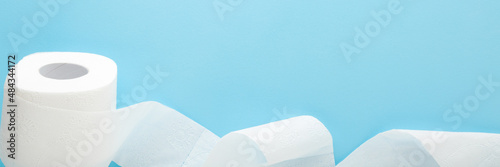Soft, white unrolled toilet paper on light blue table background. Pastel color. Hygiene concept. Empty place for text or logo. Closeup. Wide banner.