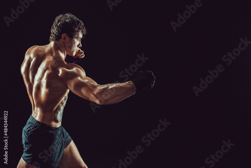 Side view of boxer in red gloves who practicing swing on black background. Sport concept 