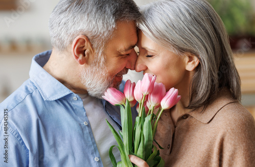 Elderly couple in love hugging on Valentine's day. A loving   husband gives his wife a  bouquet of tulip