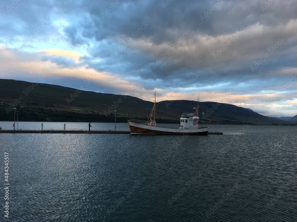 Obraz premium Boat moored at pier in Húsavík Harbor under cloud sky at sunset. Iceland.