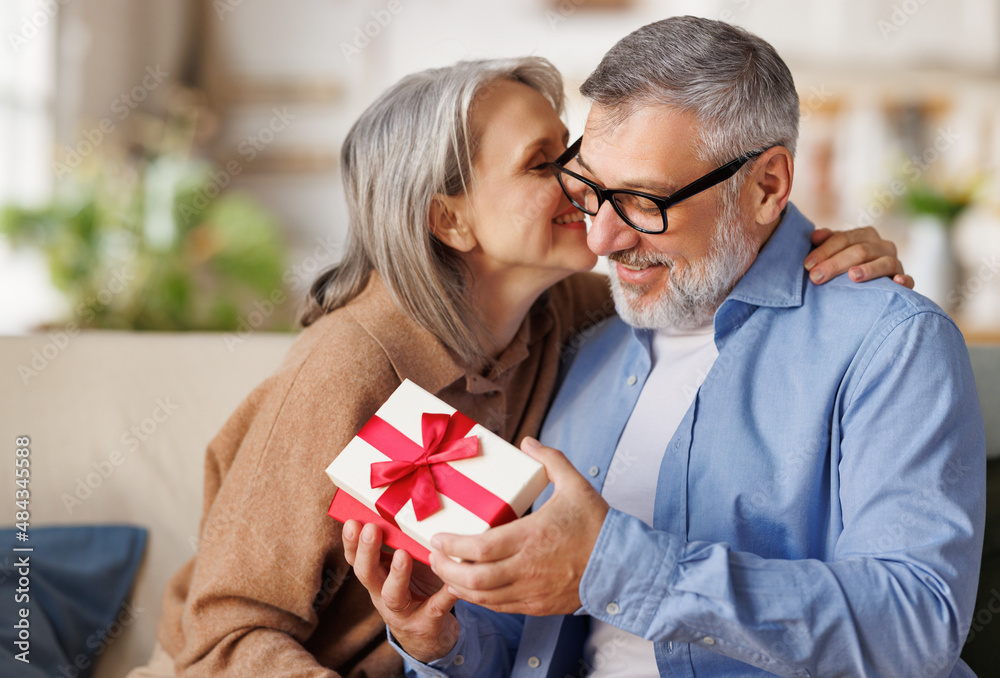 Loving woman wife giving present gift box for Valentine's day to happy surprised husband, sitting together on couch at home. Loving woman wife giving present gift box for Valentine's day to happy surprised husband, sitting together on couch at home.