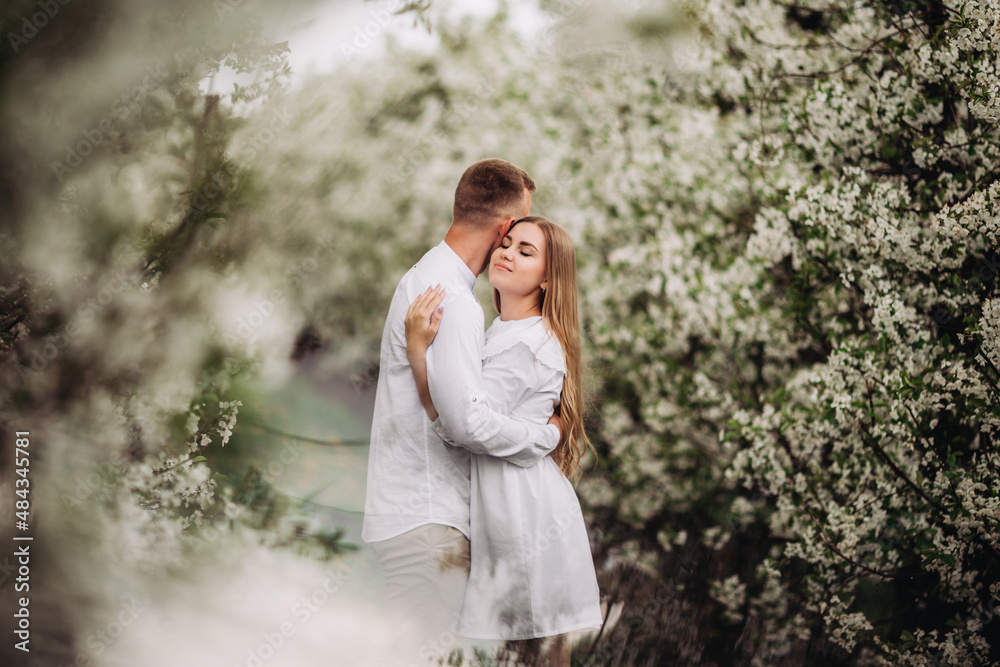 Happy family couple in love in a spring blooming apple orchard. Happy family enjoy each other while walking in the garden. The man holds the woman's hand. Family relationships Happy family couple in love in a spring blooming apple orchard. Happy family enjoy each other while walking in the garden. The man holds the woman's hand. Family relationships
