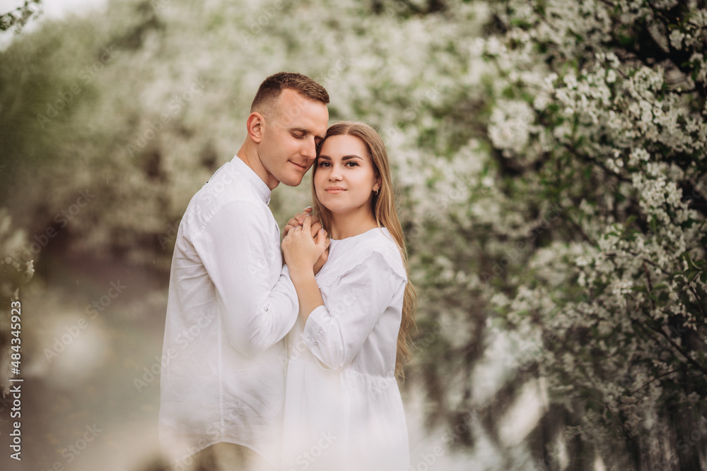 Young loving couple in a walk in a spring blooming apple orchard. Happy married couple enjoy each other while walking in the garden. Man holding woman's hand Young loving couple in a walk in a spring blooming apple orchard. Happy married couple enjoy each other while walking in the garden. Man holding woman's hand