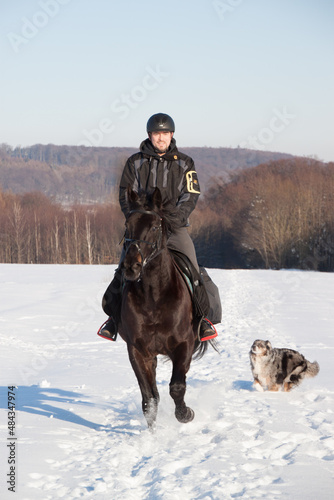 Spaß im Winter, Reiter mit Pferd macht einen Ausritt mit Hund im Schnee