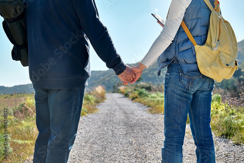Loving couple holding hands while walking on rural. Woman looking for gps for using map in her smartphone. Friendship and relationship concept. Well Being and unity with nature. Road to mountain.