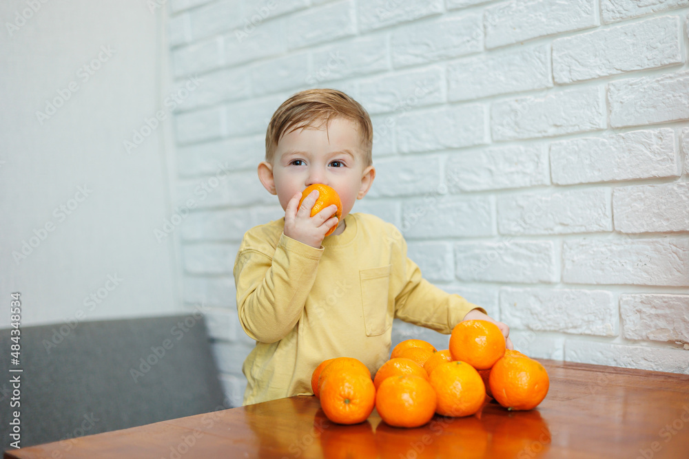 A little boy 2 years old holds tangerines in his hands. The kid wants to sit on citrus fruits for the first time. A little boy 2 years old holds tangerines in his hands. The kid wants to sit on citrus fruits for the first time.