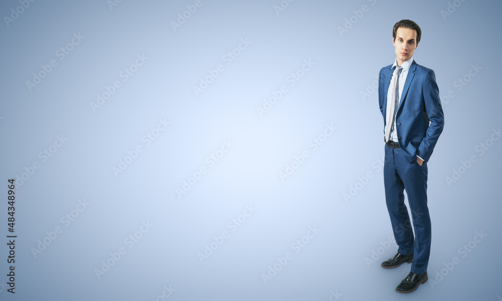 Job and recruiting concept with young businessman in blue classic suit, his hands in pockets on abstract light blue background with a space for your logo or text. Mockup Job and recruiting concept with young businessman in blue classic suit, his hands in pockets on abstract light blue background with a space for your logo or text. Mockup