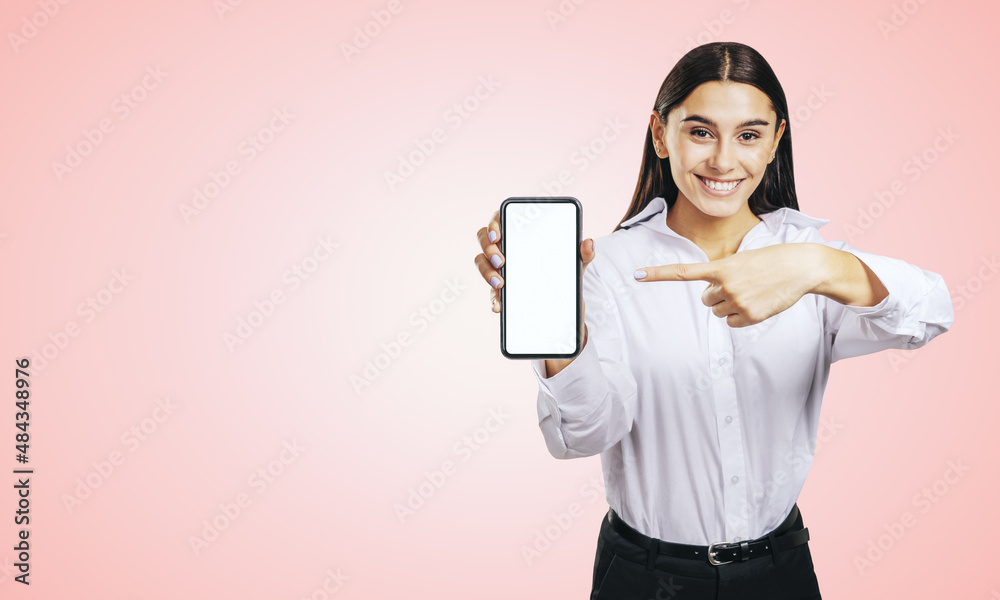 Mobile application concept with happy girl in white shirt showing modern smartphone with mockup blank white screen on abstract light pink background with copyspace Mobile application concept with happy girl in white shirt showing modern smartphone with mockup blank white screen on abstract light pink background with copyspace
