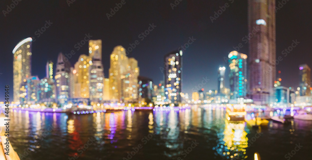 Night Skyline Abstract Boke Bokeh Background. Design Backdrop. Beautiful Night view of high-rise buildings of residential district in Dubai Marina And Tourist Boat, Sightseeing Boat Sailing On Dubai