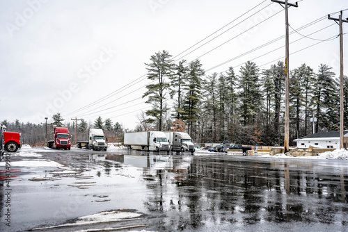 Truck stop wet winter parking lot with industrial bir rig semi trucks with semi trailers standing for truck driver rest and waiting for drivable weather