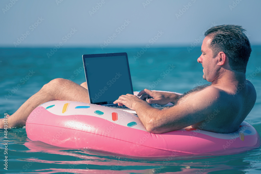 Businessman working, using laptop computer on inflatable ring in the water.