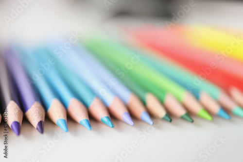 Many sharp multicolored pencils lying over colors of rainbow closeup background