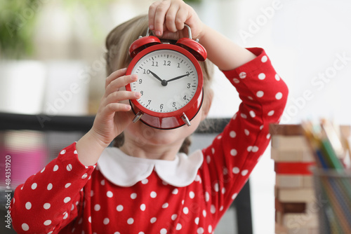 Little girl holding red alarm clock in front of her face photo