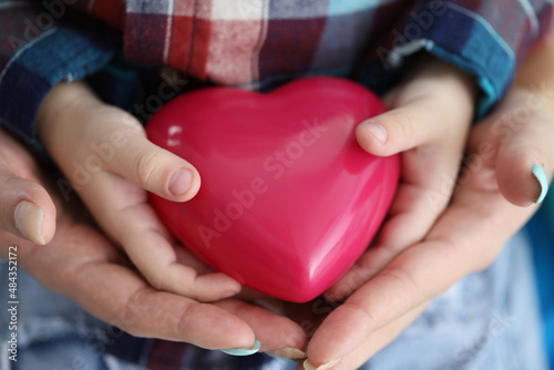 Woman and child hands holding red toy heart closeup