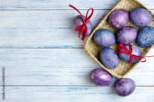 Happy Easter greeting card with eggs in trendy purple very peri color in the basket on a wooden table. Natural dye karkade tea.