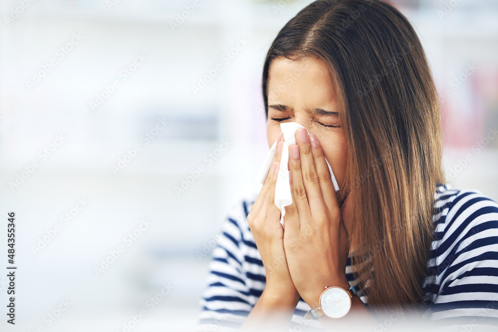 Its allergy season again. Shot of a young woman with allergies sneezing into a tissue at home. - obrazy, fototapety, plakaty 