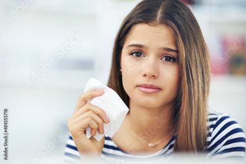 Springtime means allergies for many. Portrait of a young woman suffering from allergies holding a tissue at home.