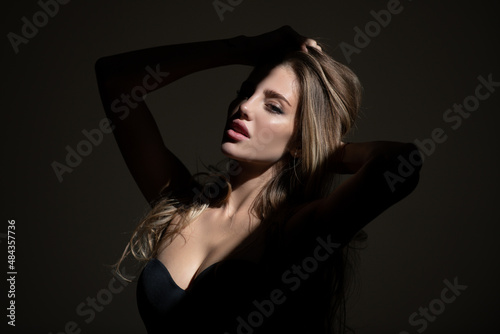 Stylish sexy woman on a gray background. Sensual young model on black studio. Sensual girl with art shadow light. Fashion portrait of elegant woman in shadow.
