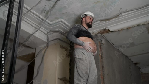 Fat bearded adult man in protective helmet and black tight fitting clothing remove construction whitewash vintage high ceiling. Overhaul repair with your own hands concept. 4k slow motion footage  photo