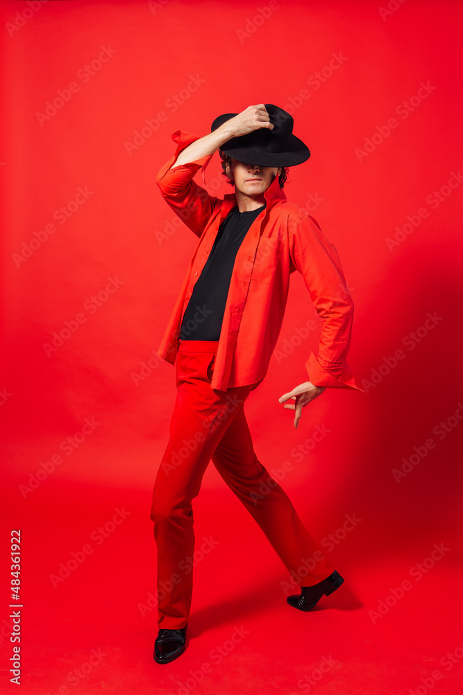 Tall handsome man dressed in red shirt and black hat posing on the red background Tall handsome man dressed in red shirt and black hat posing on the red background