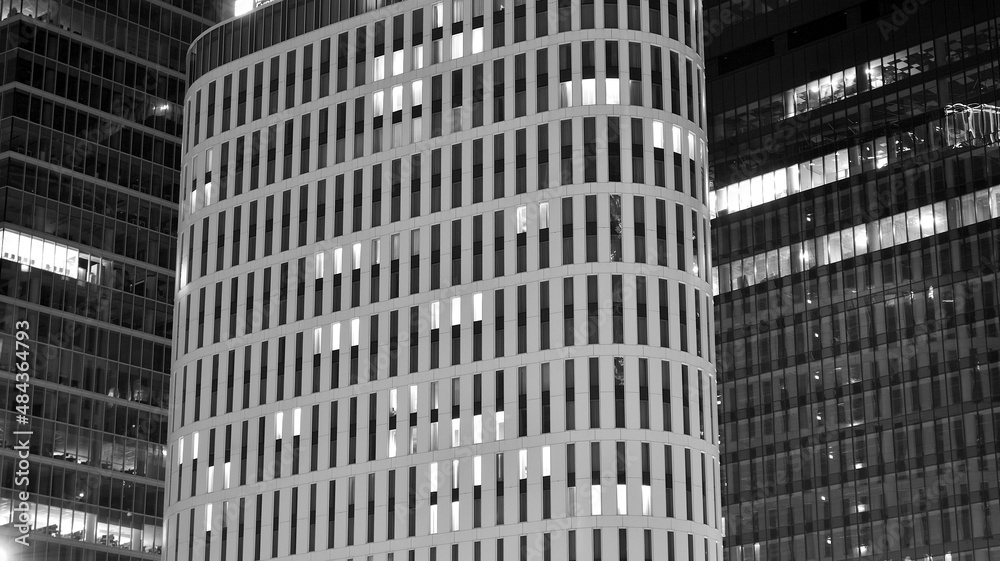 Amazing night cityscape. Office building at night, building facade with glass and lights. View with illuminated modern skyscraper. Scenic glowing windows of skyscrapers at evening. Black and white.