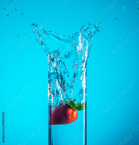 Fresh strawberry dropped into blue water with splash