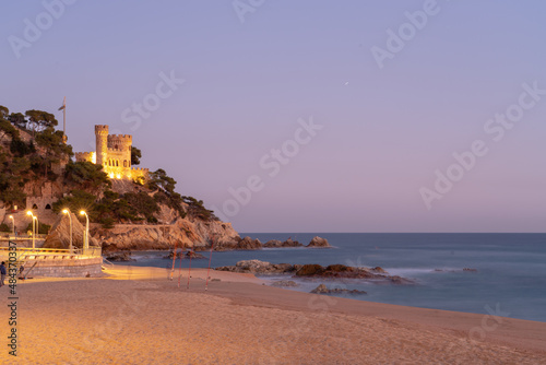 old castle on a hill by the sea at night illuminated by lanterns