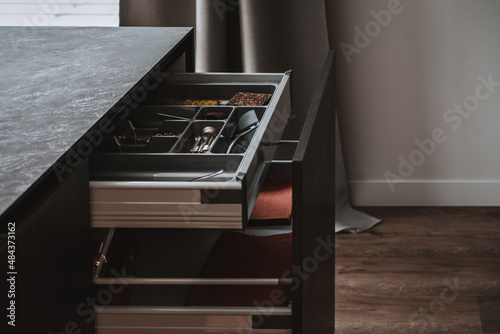 Dark grey kitchen design - detail of modern interior. Open hidden drawers with kitchenware and utensil. Soft closing inner drawer ideas.