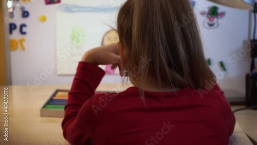 A little girl with a ponytail looks at drawings