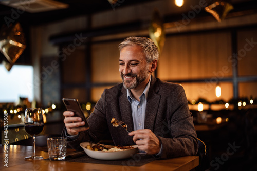 Joyful adult man, receiving a lovely message, during his meal, on his phone.
