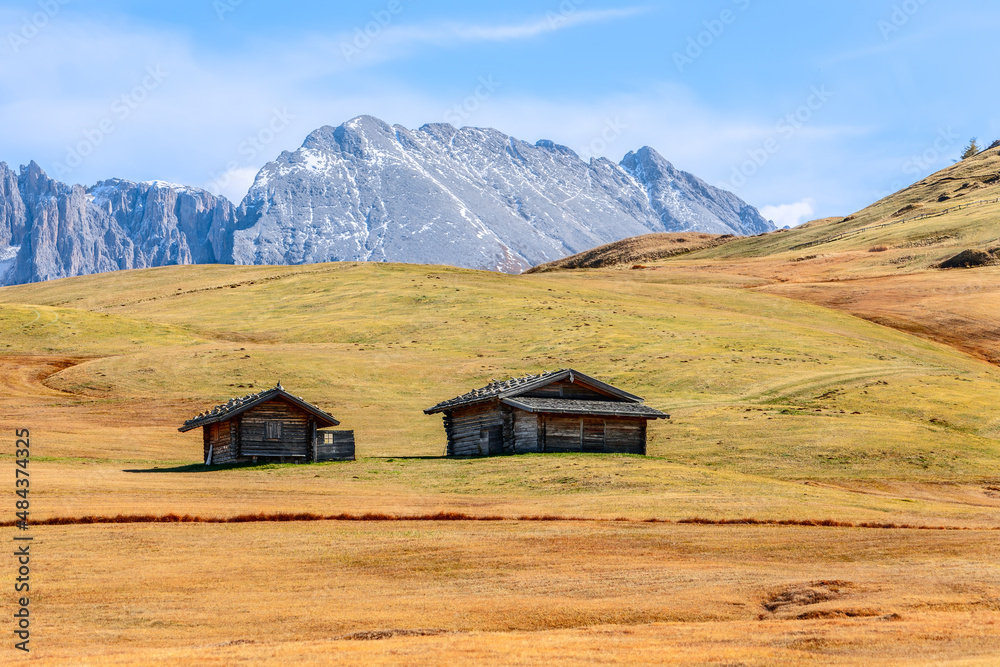 Two alpine huts on Seiser Alm plateau in autumn on the background of Langkofel Group mountains