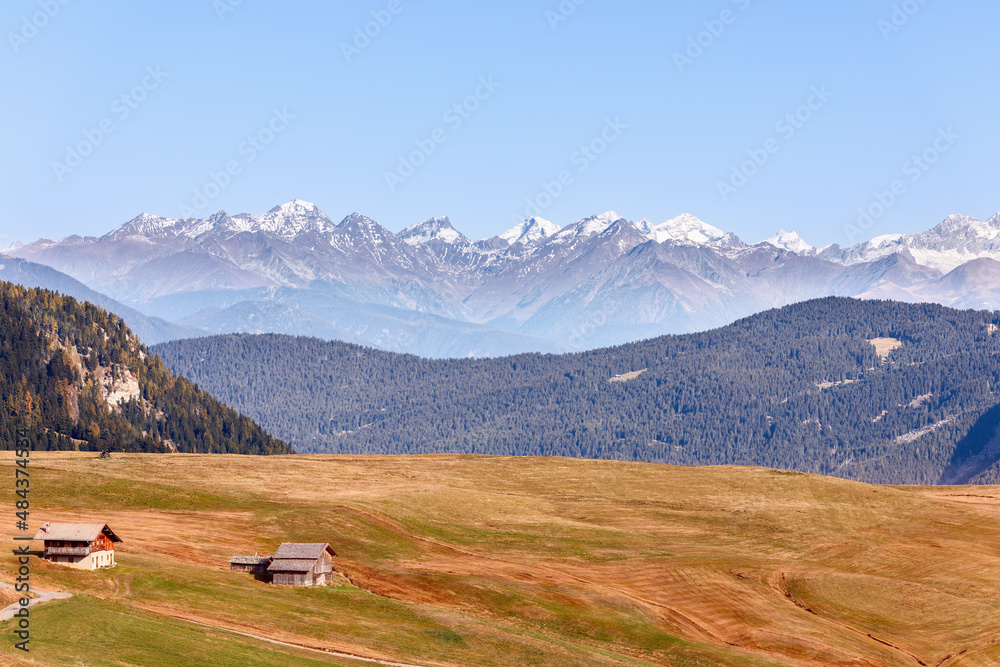 Alpine huts on the Seiser Alm plateau and snow capped peaks of the Dolomites