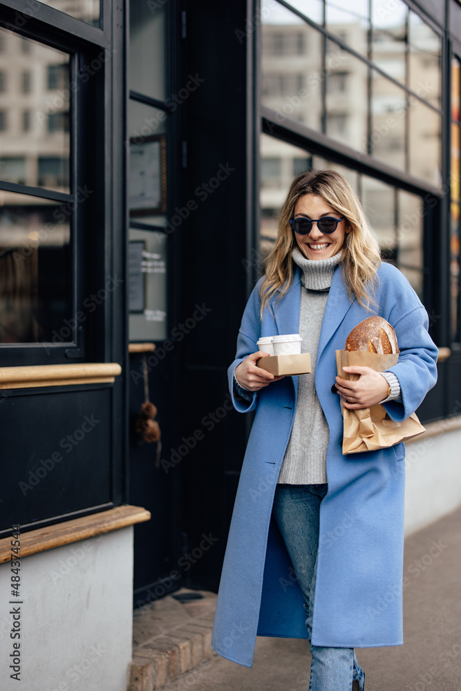 Fototapeta premium Women having a busy morning, holding cups of coffee and a loaf of bread, walking.