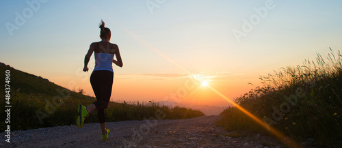 woman running on a mountain trail at summer sunset banner size