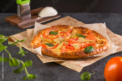 Traditional pizza Margherita with tomatoes, basil and mozzarella cheese close-up parchment paper on a dark background. Delicious fresh and homemade fast food.