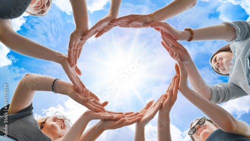 Friends make a circle from their palms against the background of a fabulous sky.