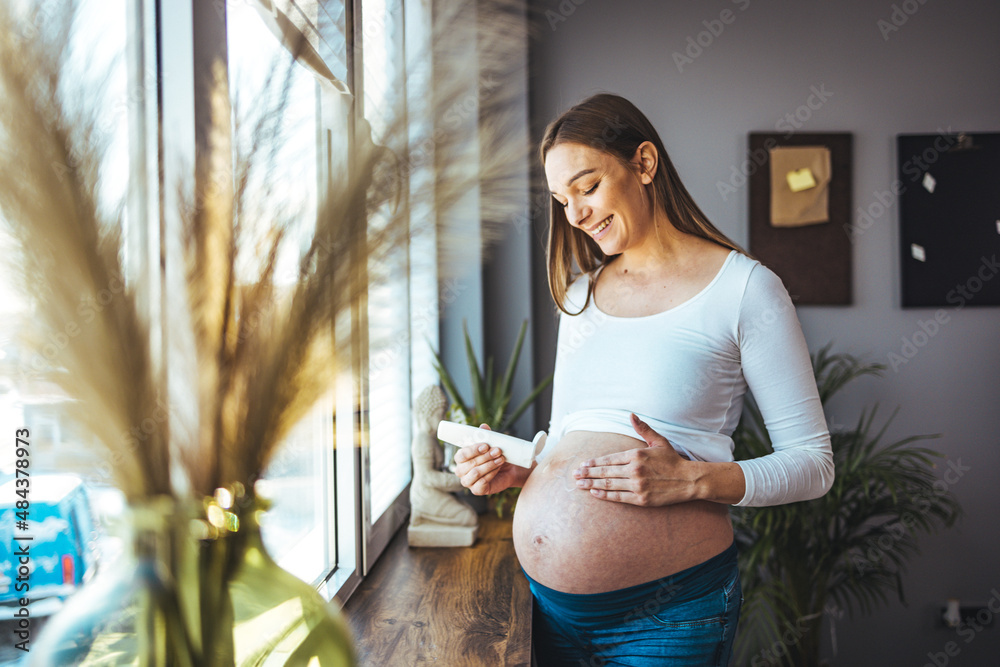 Pregnant woman applying moisturizer cream on her belly against stretch