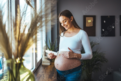 Pregnancy, people and maternity concept - Close up of pregnant woman applying stretch mark cream to belly. 